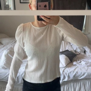 Vit långärmad tröja från Lindex - En vit långärmad tröja från Lindex med en ribbad struktur. Tröjan har en öppen rygg med knytning och puffiga ärmar.