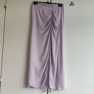 Långkjol - Ljuslila långkjol från KappAhl i storlek 34. Har en slit fram/på sidan lite beroende på hur man väljer att bara kjolen. Dragkedja i sidan vid midjan. Tunn och luftig, perfekt till sommaren! Något sliten längst ned och vid midjan (se bilder)