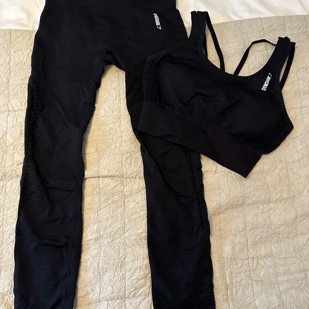 Ett svart träningsset från Gymshark bestående av en sport-bh och leggings. Setet är tillverkat i ett stretchigt och bekvämt material med andningsfunktion. Leggingsen har ett hålmönster längs benen och sport-bh:n har breda axelband för extra stöd. Nypris 920:- för setet, mitt pris 450:-. I nyskick! . Sportswear.