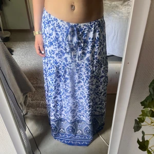 Blå och vit långkjol - En vacker långkjol med blått och vitt blommönster. Kjolen har ett knytband i midjan.