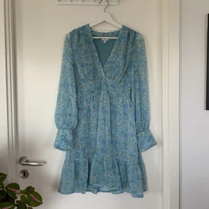 Klänning - Blommig klänning i blott och volanger! Fina och tunna ärmar, v-ringning, fin passform! Använd ett fåtal gånger, men är i mycket fint skick!