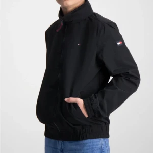 Tommy Hilfigher vindjacka  - Nyskick! Oanvänd. Stl 164/14år  Svart. Perfekt vår & sommar & höstjacka! Välj själv om du vill ha luvan eller inte då den går att rulla in i kragen. Nypris 1100 kr