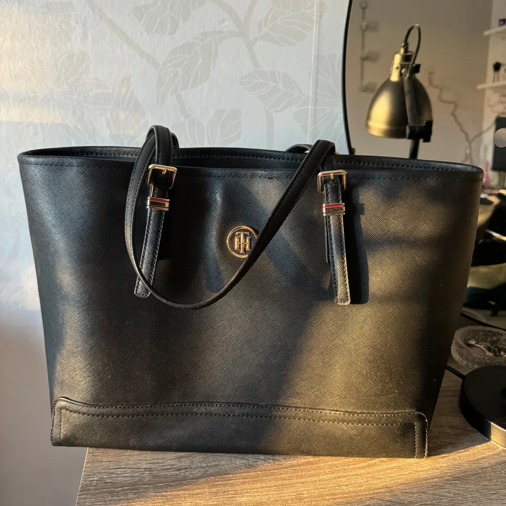 Tommy Hilfiger, äkta handväska svart I nyskick!  Mått-  Höjd: 28 cm i storlek Längd: 34 cm i storlek Vidd: 14 cm i storlek Handtag: 20 cm i storlek . Väskor.