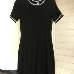 Ribbad klänning - Svart ribbad klänning med vita detaljer. Storlek 40. Oanvänd med prislappen kvar.