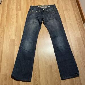 (9) lågmidjade bootcut jeans med gul brodering på fickorna, från cron x. Midjemått över: 34 cm, innerbenslängd 81 cm 🩵