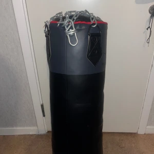 Boxningsäck - Boxningssäcken väger 25kg och är 30cm bred och 90cm lång. Den kommer med handskar och är aldrig använd.