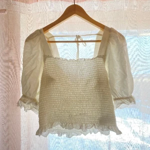 Snygg vit blus till sommaren 🐚 - Den är ryschad framtill och har fina ärmar. Kan knytas baktill för mer fast passform. Man känner sig as fin i den😊