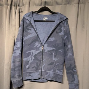 Ralph Lauren Hoodie - Ralph Lauren Camo Hoodie i blå. Skicket är ungefär 7/10 finns tecken på användning samt slitage på höger arm och en liten defekt på fickan som smälter in med camouflagen därab priset.  Storlek S. Tveka inte att höra av er om ni har några funderingar🤩