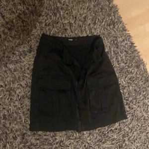 Svart tjol  - Det är en svart tjol med fickor där fram. En fickor på varje sida