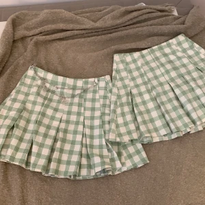 Grön och vit rutig kjol från Bershka - Två korta grön och vit rutiga kjolar från Bershka. Ena kjolen har ett dekorativt kedjebälte med fjärilar. Går att köpa ihop och separat. 1 för 50, 2 för 100kr