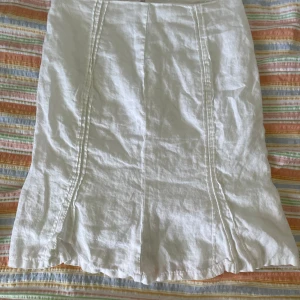 Vit kjol från Adagio - En vit kjol från Adagio. Kjolen har en enkel design med sömmar som löper vertikalt längs framsidan och baksidan. Den är knälång och har en rak passform.