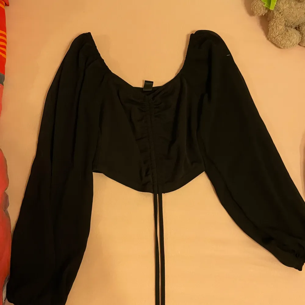 En elegant svart off-shoulder topp med långa ärmar och en snörning framtill. Toppen har en lös passform och är perfekt för festliga tillfällen. Skriv gärna om ni har frågor 💕. Yläosat.