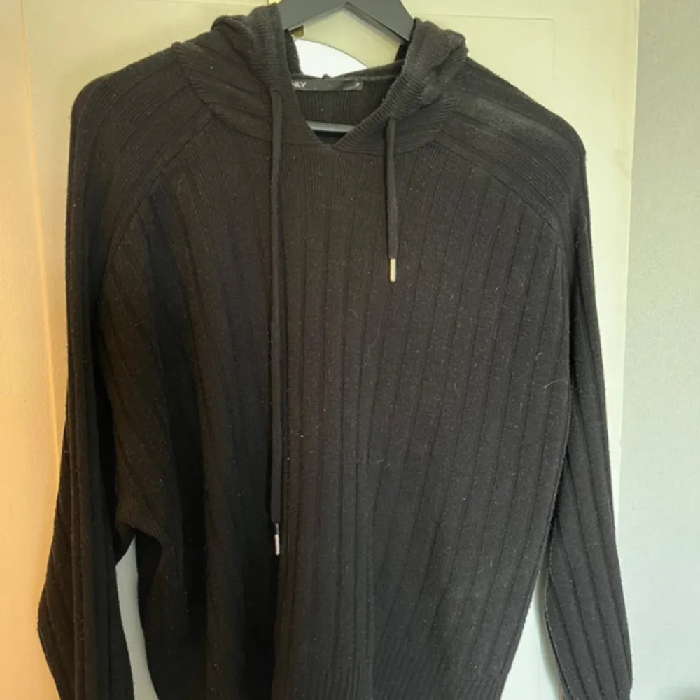 En svart stickad hoodie från ONLY med långa ärmar och ribbstickad design. . Neuletakit & Villapaidat.