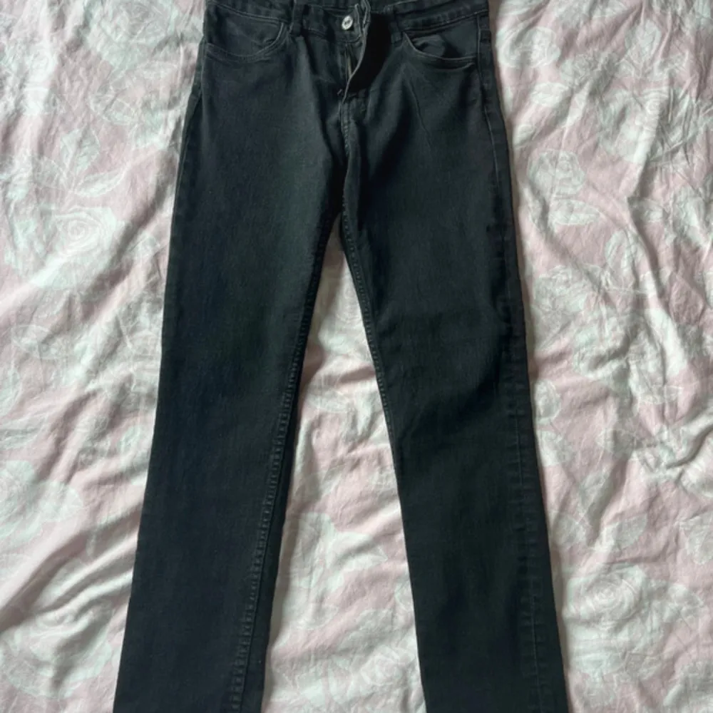 Ett par svarta skinny jeans i storlek 152. Byxorna har en klassisk femficksdesign och är tillverkade i denim. De har en knapp- och dragkedjestängning framtill.. Jeans & Byxor.