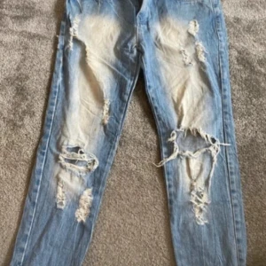 Ljusa slitna jeans - Ett par ljusa jeans med slitningar och hål på framsidan och baksidan. Jeansen har en normal passform och är tillverkade i denim. 