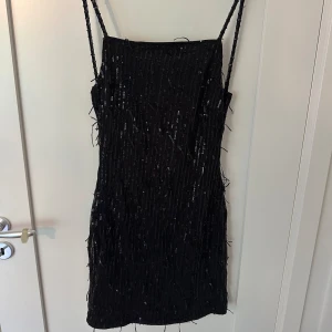 Glittrig klänning - Svart glittrig klänning med fransar och öppen rygg😊 använd en gång bara.