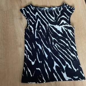 Svart och vit mönstrad topp - jättesnygg kropppassad topp med svart och vit mönster. Toppen har en rund halsringning och är tillverkad i ett stretchigt material.