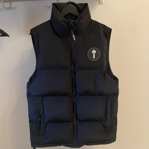 Trapstar Irongate T badge Vest Black - Köpt för ett litet tag sedan men används inte längre. Finns inga skador eller fläckar på västen då jag använt den ett fåtal gånger. Så gott som ny! Storlek S men passar mig bra även fast jag har storlek M i de flesta plagg