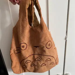 En liten väska/påse med studio ghibli figuren Totoro. Är i brunt Manchester tyg utåtvändigt och har måtten 32/28cm. 