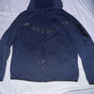 Mörkblå hoodie från Nike - Säljer en mörkblå hoodie från Nike i barn storlek L. Den har en dragkedja framtill och en praktisk ficka med dragkedja på ärmen. Perfekt för höst och vår, med en stilren design och bekvämt material.lite smutsig men går och tvätta bort