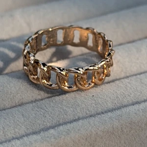 Guldfärgad kedjering - Säljer en supercool guldfärgad ring med ett kedjemönster. Ringen har en unik design med öppna länkar som ger den en modern och edgy look. Perfekt för att ge lite extra bling till din outfit!