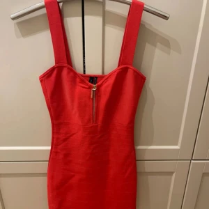 Röd klänning med dragkedja - Säljer en snygg röd bandageklänning från Guess Marciano med dragkedja framtill. Den är ärmlös och har breda axelband, vilket ger en stilren look. Perfekt för festliga tillfällen! Storlek M men passar även S. 