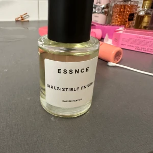 Essnce Irresistible Enigma Eau de Parfum - Säljer en flaska Essnce Irresistible Enigma Eau de Parfum. Den har en fräsch och fruktig öppning med toppnoter av päron, mandarin och bergamott. Hjärtat av doften består av apelsinblomma och sambac jasmin, medan basen är varm och omfamnande med bourbon vanilj, vit mysk, amber och benzoin. Perfekt för alla tillfällen och klassas som en 'mass appealing' doft. Flaskan är stilren med en enkel design och svart kork. påminner om Prada paradoxe