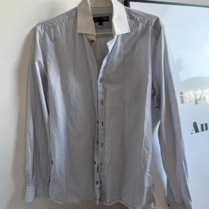 Vit och blå randig skjorta i egyptisk bomull - Säljer en  vit och blå randig skjorta i Egyptian Cotton från Dressman. Skjortan är i storlek M och har långa ärmar och knappar framtill. Skjortan är i superfint skick