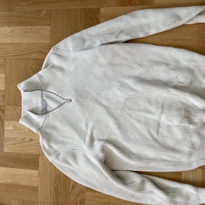 Vit stickad tröja från Zara - Säljer en stilren och mysig vit stickad halfzip tröja från Zara. Den har en dragkedja vid halsen och är perfekt för kyligare dagar. Tröjan är långärmad och har en klassisk passform. Perfekt för både vardag och lite finare tillfällen!