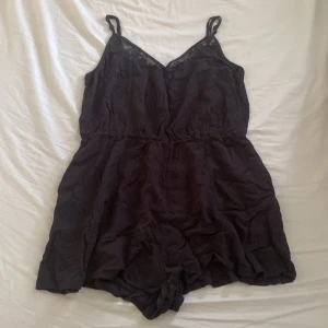 Svart ärmlös jumpsuit med spetsdetaljer - säljer en svart ärmlös jumpsuit typ med justerbara axelband och spetsdetaljer vid halsringningen. vet tyvär inte vilket märke den är ifrån.