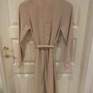 Säljer en snygg beige trenchcoat från 157. Den har en klassisk design med ett bälte i midjan för en fin passform. Perfekt för vår och höst! Långärmad och i ett stilrent utförande.