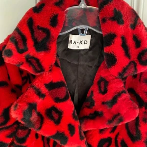 Pälsjacka NA-KD strl 34/XS - En röd/svart leopardmönstradpälsjacka, använd fåtal gånger. Knäpps med hjälp av två knappar som är fungerande, finns två fickor.   I storlek 34/XS