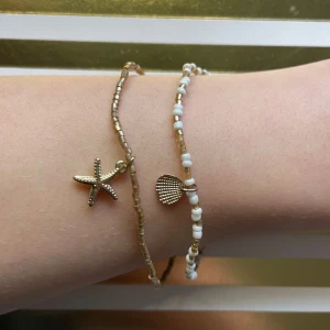 Två armband med havstema - Säljer två fina armband med havstema. Det ena armbandet har vita och guldiga pärlor med ett snäckskalshänge, och det andra har guldiga pärlor med ett sjöstjärnehänge. Perfekta accessoarer för sommaren.säljer båda tillsamman men om du bara vill köpa en är det bara och kontakta