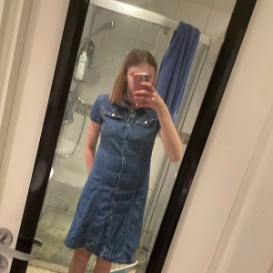 Jeansklänning  - Säljer en jeansklänning från h&m i storlek 164 men passar XS/S. Jeansklänningen har 2 fickor framtill och är lite mellan blå i färgen. Den har även knappar nästan hela vägen ner framtill samt en öppen slits nertill både bak men även framm. Klänningen är i bra skick och gjord i ett tunnare jeans tyg. 💕