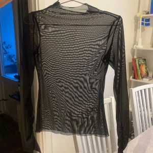 Svart genomskinlig topp - Säljer en svart långärmad meshtröja. Perfekt för lager-på-lager eller som statement-plagg. Tröjan har en tight passform och är tillverkad i ett lätt och luftigt material.