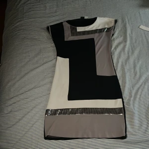 Svart och vit klänning från Bodyflirt - Snygg klänning från Bodyflirt i svart och vit med geometriskt mönster. Klänningen har korta ärmar och dekorativa paljettdetaljer som ger en glittrig touch. Perfekt för en stilren look.