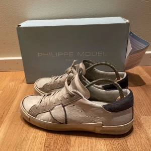 Philippe model skor - Snygga vita sneakers från Philippe model. Har ett litet hål i hälen som kan limmas med ett super lim innan den postas. Även nån liten repa på skon. Box och papperserikett kommer med. Storlek 40, passar 0,5 storlek större