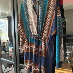 Mönstrad klänning från Boohoo - Säljer en färgglad och mönstrad klänning från Boohoo i storlek EU 42. Klänningen har ett unikt mönster i turkos, brun och orange med långa ärmar och knytning i midjan. Perfekt för att sticka ut med stil!