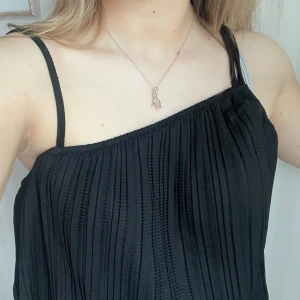 Svart asymmetriskt linne - Snyggt svart asymmetriskt linne med smala axelband och ett stilrent plisserat mönster. 