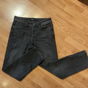 Svarta jeans från Jack & Jones - Snygga svarta jeans från Jack & Jones med en tapered passform. De har en klassisk femficksdesign och knappar i midjan. Perfekta för en stilren look. Storlek 29/30