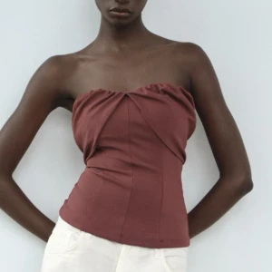Vinröd tubtopp från Zara - Snygg vinröd tubtopp från Zara i ett stilrent och elegant snitt. Toppen är axelbandslös och har en draperad design framtill som ger en unik look. Perfekt för att skapa en chic outfit.