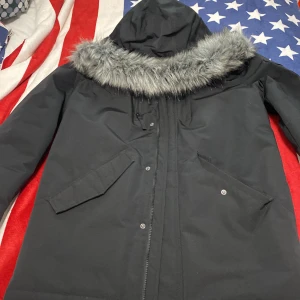 Svart parkajacka från Primark - Säljer en svart parkajacka från Primark med huva och fuskpälsdetalj. Jackan har långa ärmar och praktiska fickor framtill. Perfekt för kyliga dagar med sin stilrena design och varma material.