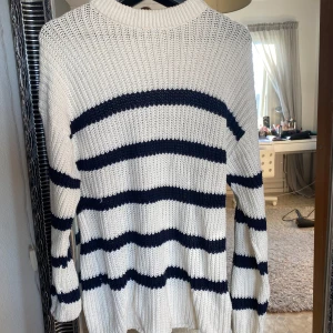 Vit och marinblå randig stickad tröja - Säljer en mysig vit stickad tröja med marinblå ränder. Tröjan har långa ärmar och en rund halsringning. Perfekt för kyligare dagar. Hör av dig vid intresse! 💙Den har några inperfektioner såsom en fläck längre ned på tröjan. Lite färgade armar vid handlederna och liten skarv i stickningen.