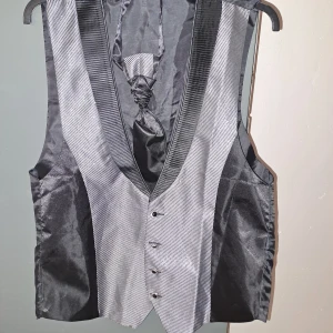 Svart och grå väst med knappar - Elegant svart och grå väst med knappar framtill och en subtil randig design. Perfekt för en stilren look. Västen har en klassisk passform och en snygg krage.