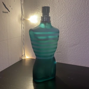 Parfymflaska i form av en manlig torso - Säljer en ikonisk parfymflaska formad som en manlig torso i frostat glas med turkosa och blå ränder. Flaskan har en unik design och är perfekt för den som vill ha något annorlunda på hyllan. Den har en metallisk spraytopp.
