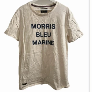 Vit t-shirt från Morris - Snygg vit t-shirt från Morris med texten 'Morris Bleu Marine' i blått på framsidan. Perfekt för en avslappnad stil. T-shirten har en klassisk rund hals och korta ärmar.