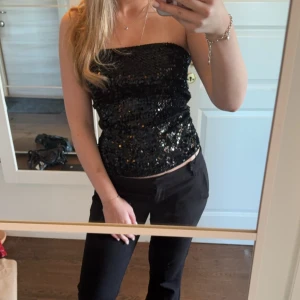 Svart paljettubtopp - Snygg svart tubtopp med glittrande paljetter. Perfekt för en kväll ute eller fest. Den är axelbandslös och har en tight passform som framhäver figuren!Säljer även jeansen på sista bilden💋💘