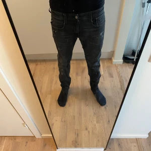 Svarta replay med slitningar - Snygga svarta replay jeansbyxor med en slim passform. De har en klassisk femficksdesign och knappar i midjan. Perfekta för en stilren look. Säljer för att jag inte använder de längre. Köpta för 1299