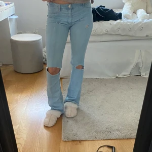 Ljusblå jeans med utsvängda ben från H&M - Säljer ett par ljusblå lågmidjade bootcut jeans från H&M med hål på knäna. Så snygga och i väldigt bra skick. Lite missfärgade längst ner men inget man tänker på!