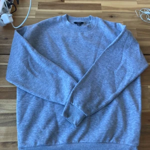 Grå sweatshirt från Smog - Säljer en grå sweatshirt från Smog i storlek M. Tröjan har en relaxed fit och är tillverkad av en blandning av bomull och polyester. Perfekt för en avslappnad stil med ribbade muddar vid ärmslut och nederkant.